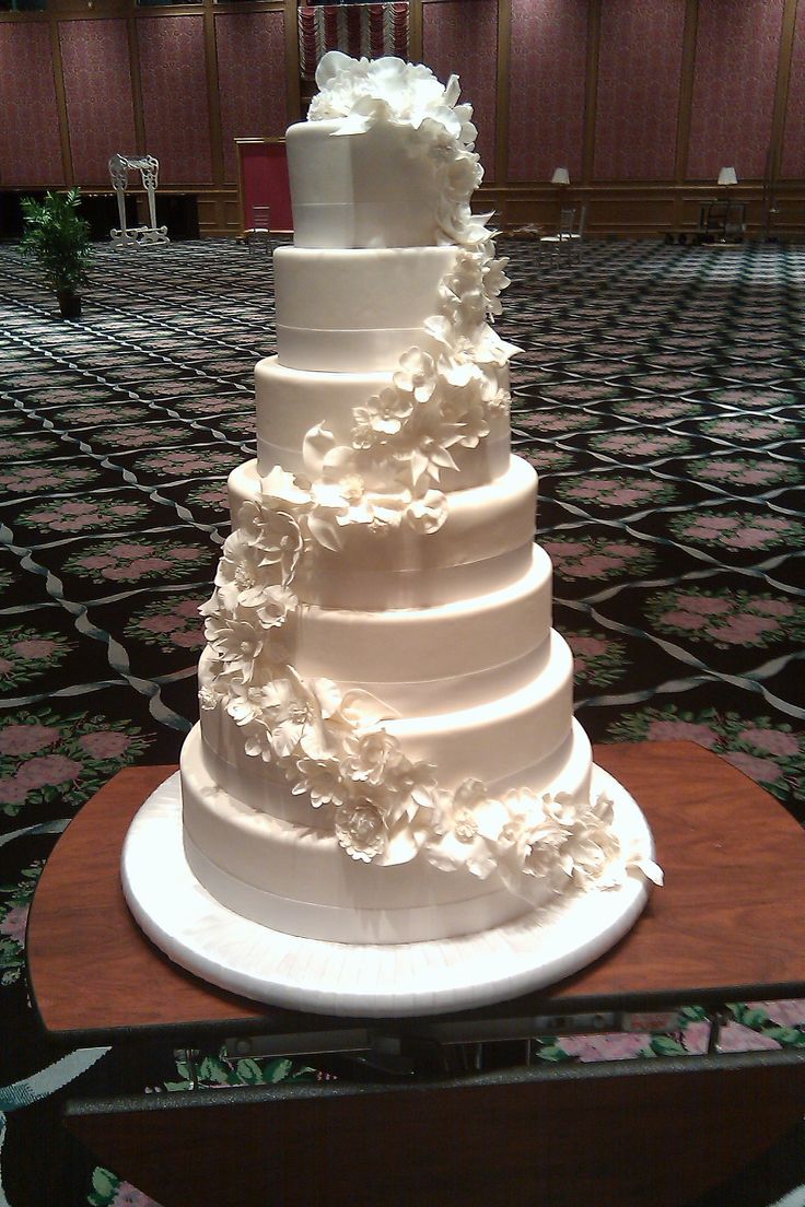 A classic multi-tiered white wedding cake with intricate frosting details sits untouched on a decorated table, symbolizing the traditional wedding cake custom that many modern couples are choosing to skip in favor of more creative and guest-friendly dessert alternatives.