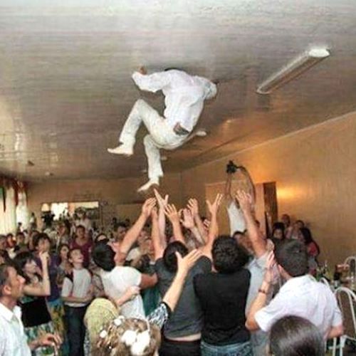 A groom with his head playfully stuck in a low ceiling beam after being tossed into the air by his groomsmen, capturing a humorous moment that puts a lighthearted twist on traditional wedding reception celebrations and shows how couples are making wedding traditions their own.