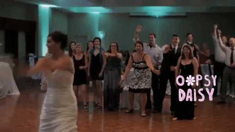 A bride tosses her bouquet over her shoulder at a wedding reception while a guest stumbles and falls over trying to catch it, humorously highlighting how some wedding traditions, like the bouquet toss, can create more awkward moments than cherished memories.