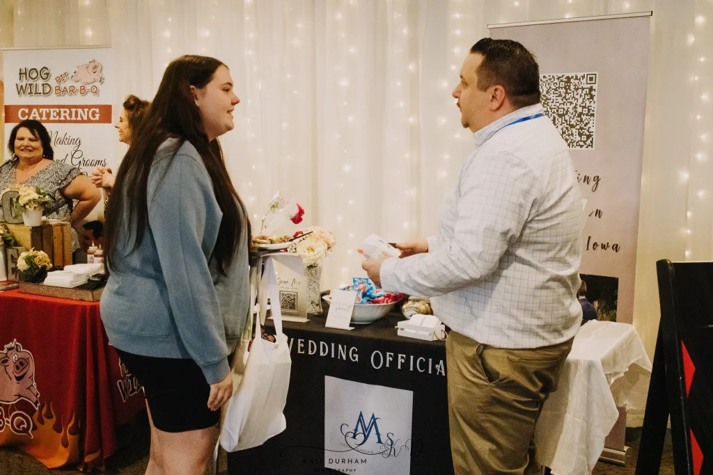 Engaged couples speaking with vendors at a Nebraska bridal fair, illustrating how much value vendors can gain by exhibiting at a bridal expo.