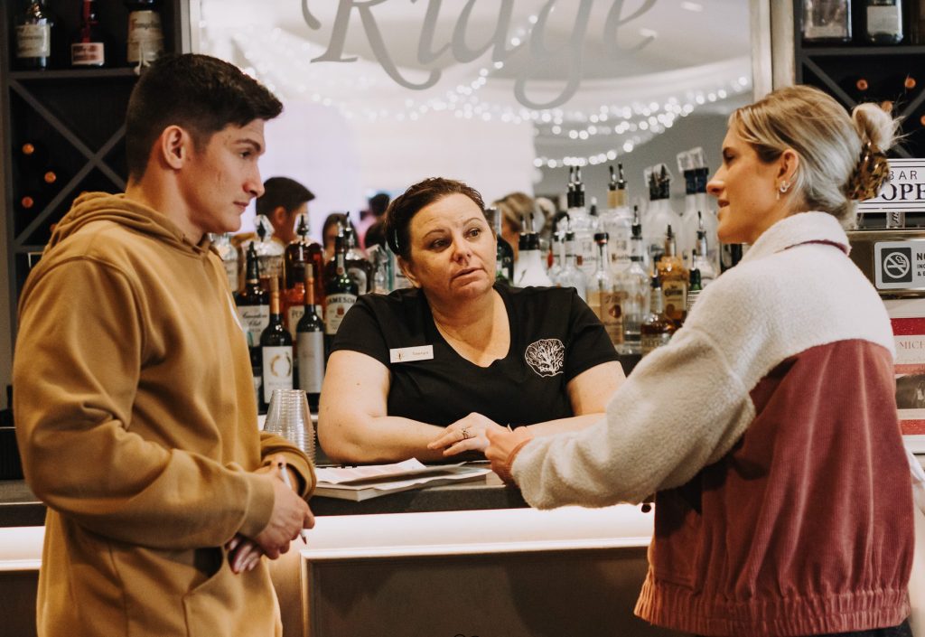 IMG_4743 Couple speaking with a vendor behind the bar at a wedding expo, showcasing real conversations and vendor connections during the Heartland Wedding Fair.